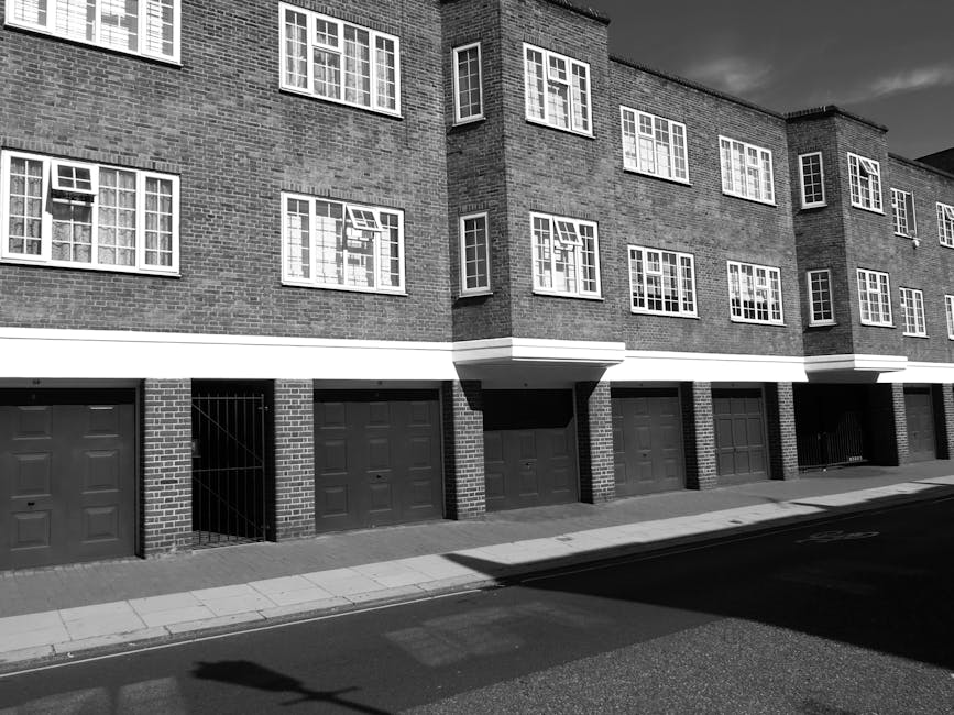 The image shows a wide, multi-storey white residential building with ornate architectural details, including decorative moldings and balconies with wrought iron railings, situated on a city street. In